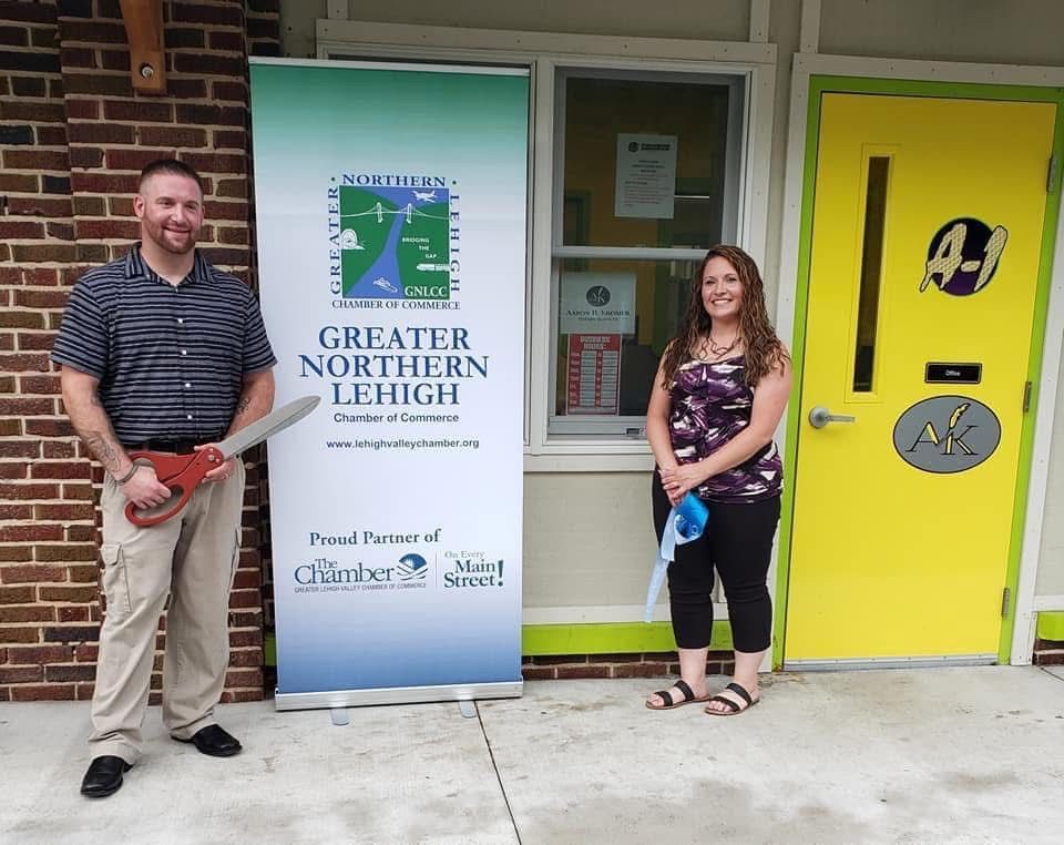 Aaron and a woman outside the office with the bright yellow AK door and Greater Northern Lehigh Chamber of Commerce banner